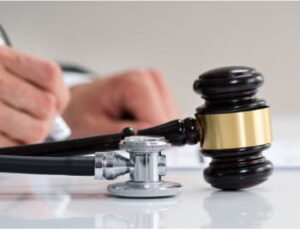 A gavel and a stethoscope rest on a table, with a person writing in the background.