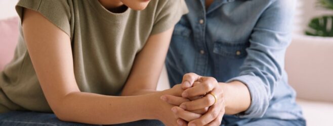 A man and woman sit close together, hands clasped, and only the woman's face is showing.