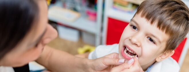 A young child sitting in a dentist's office with a dentist examining his teeth.