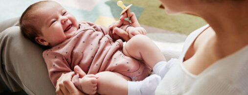 A smiling baby looks up at their mom or caregiver.