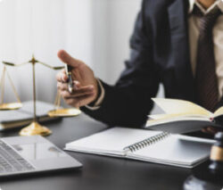 Lawyer sitting at a desk with an open notebook, a laptop, and scales of justice.